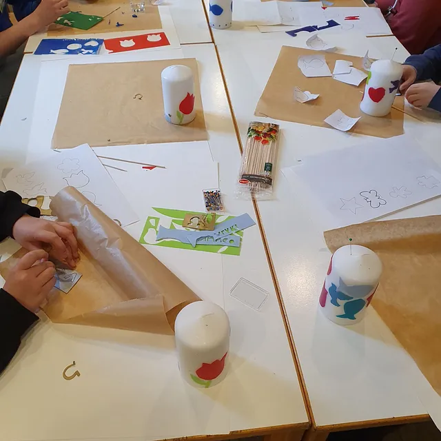 Kinder am Tisch beim Verzieren von Kerzen mit bunten Wachsmotiven.