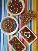 Verschiedene Schokoladen-Leckereien, verziert mit bunten Bonbons und Marshmallows auf einer gestreiften Tischdecke.