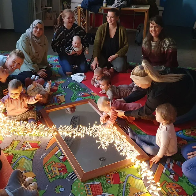 Mütter und Babys sitzen im Kreis um Lichter in einem Gemeindesaal.