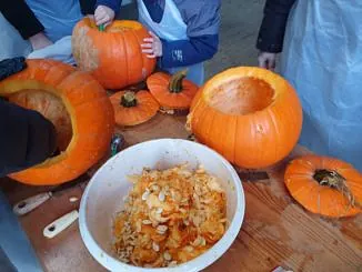 Kinder und Erwachsene beim Aushöhlen von Kürbissen an einem Tisch in der Gemeinde.