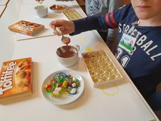 Ein Kind gießt mit einem Löffel Schokolade in Pralinenformen während eines Gemeindeworkshops.