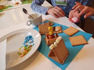 Ein Kind bastelt ein kleines Haus aus Keksen und Süßigkeiten in einem Gemeindeworkshop.