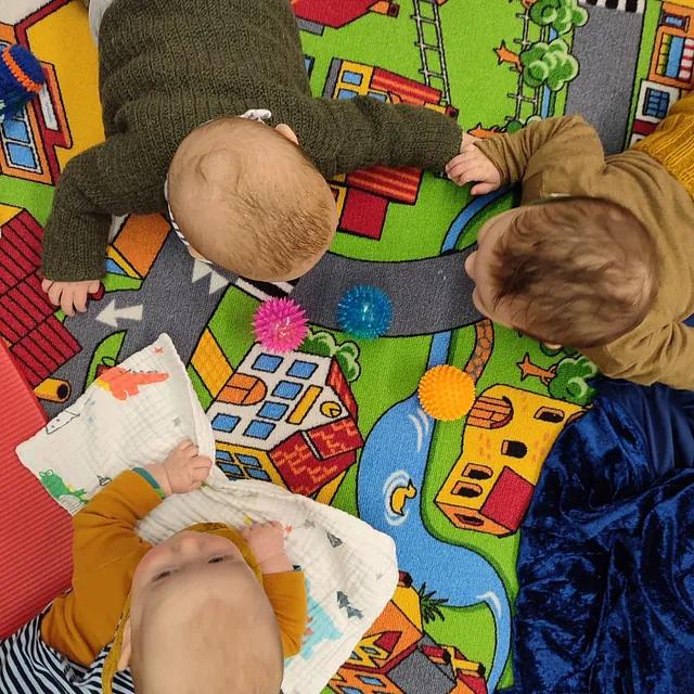 Babys spielen gemeinsam auf einer bunten Spielmatte in der Gemeinde.