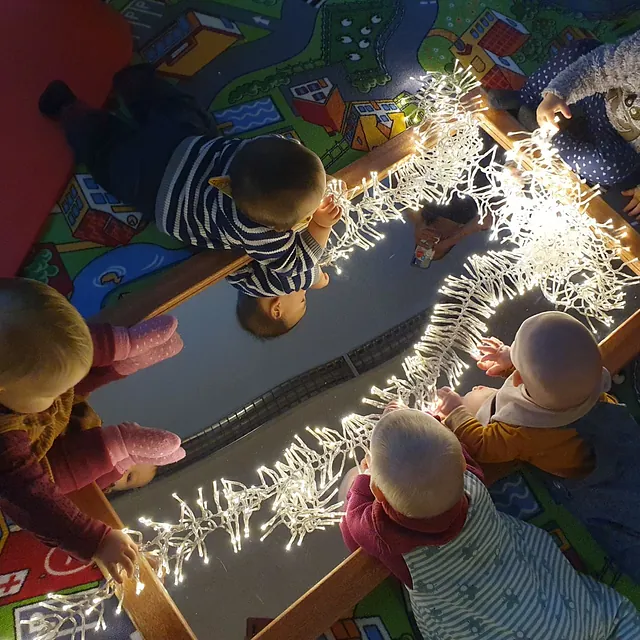 Kleinkinder entdecken eine leuchtende Lichterkette auf einem Spiegel.