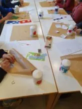 Eine Gruppe von Kindern sitzt an langen weißen Tischen und dekoriert Stumpenkerzen mit bunten Wachsmotiven.