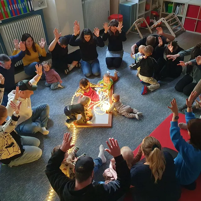 Eltern und Kleinkinder im Kreis um Lichter während einer Krabbelgruppe.