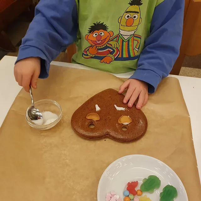 Ein Kind beim Verzieren eines Lebkuchenherzens mit Guss und Süßigkeiten.