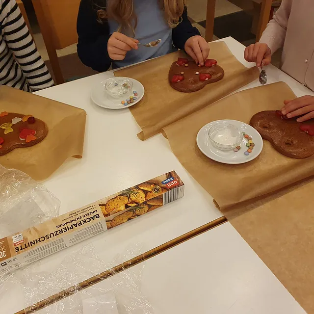Kinder verzieren Lebkuchenherzen mit Süßigkeiten in einer Gemeindegruppe.