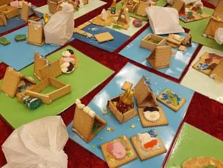 Nahaufnahme von selbstgebastelten Lebkuchenhäusern aus Keksen und Süßigkeiten auf buntem Papier.